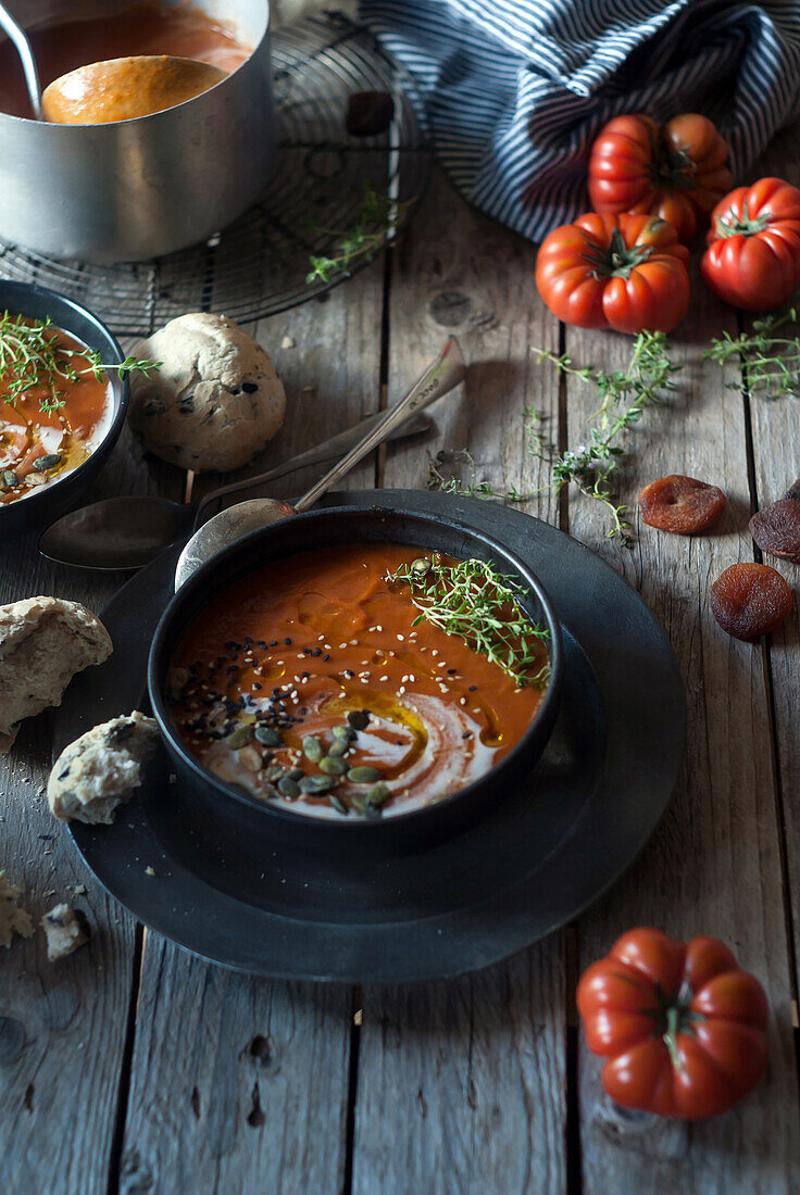 Composition of served bowls with delicious tomato creamy soup with seeds on table with tomatoes and bread buns