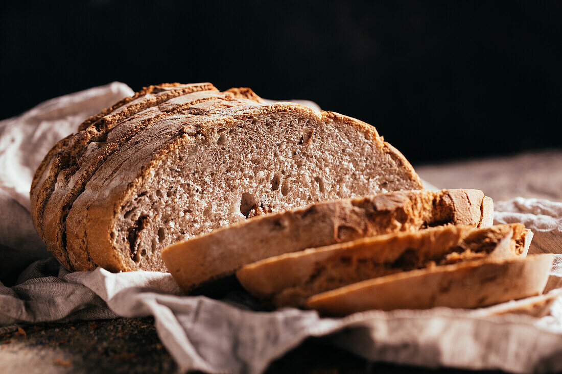 Scheiben von frisch gebackenem Vollkornbrot auf altem, schäbigem Holztisch in der Küche verstreut