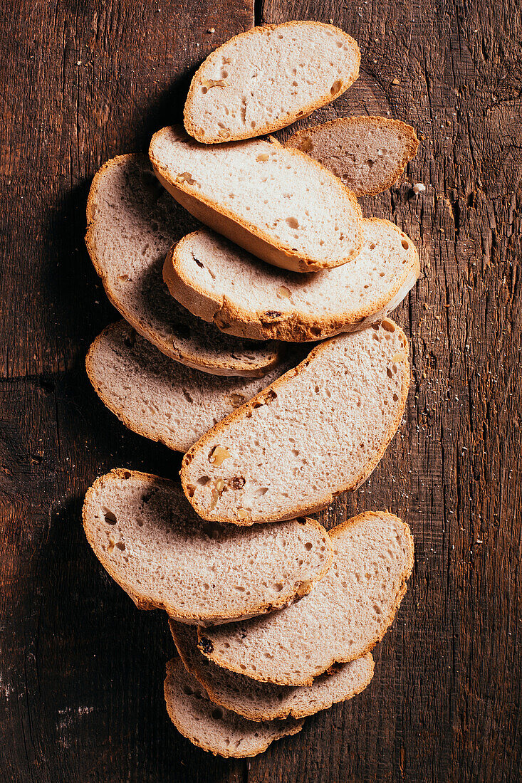 Von oben auf Scheiben von frisch gebackenem Vollkornbrot, die auf einem alten, schäbigen Holztisch in der Küche verstreut sind