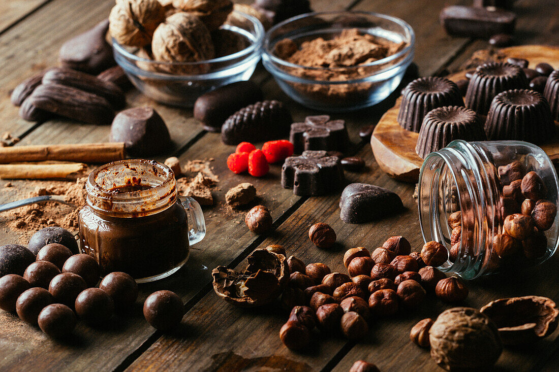 Various handmade chocolates with nuts arranged on wooden table with peanut butter and cinnamon sticks