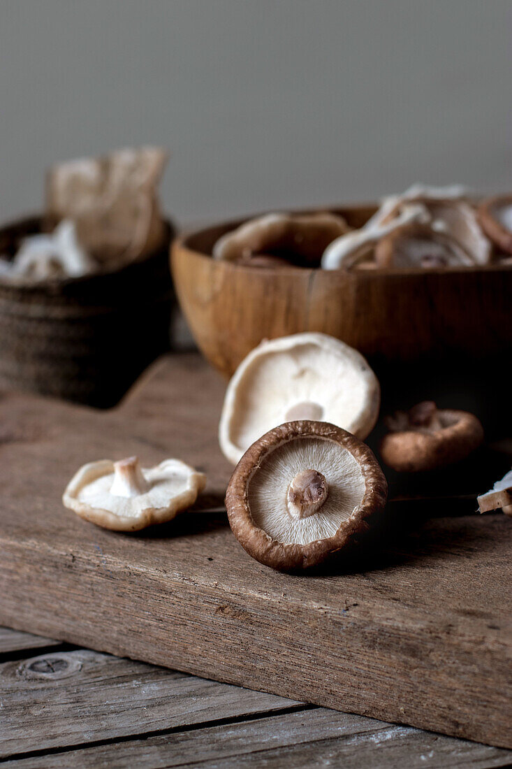 Top view of wooden bowl full of shiitake mushrooms on wood table with knife on top