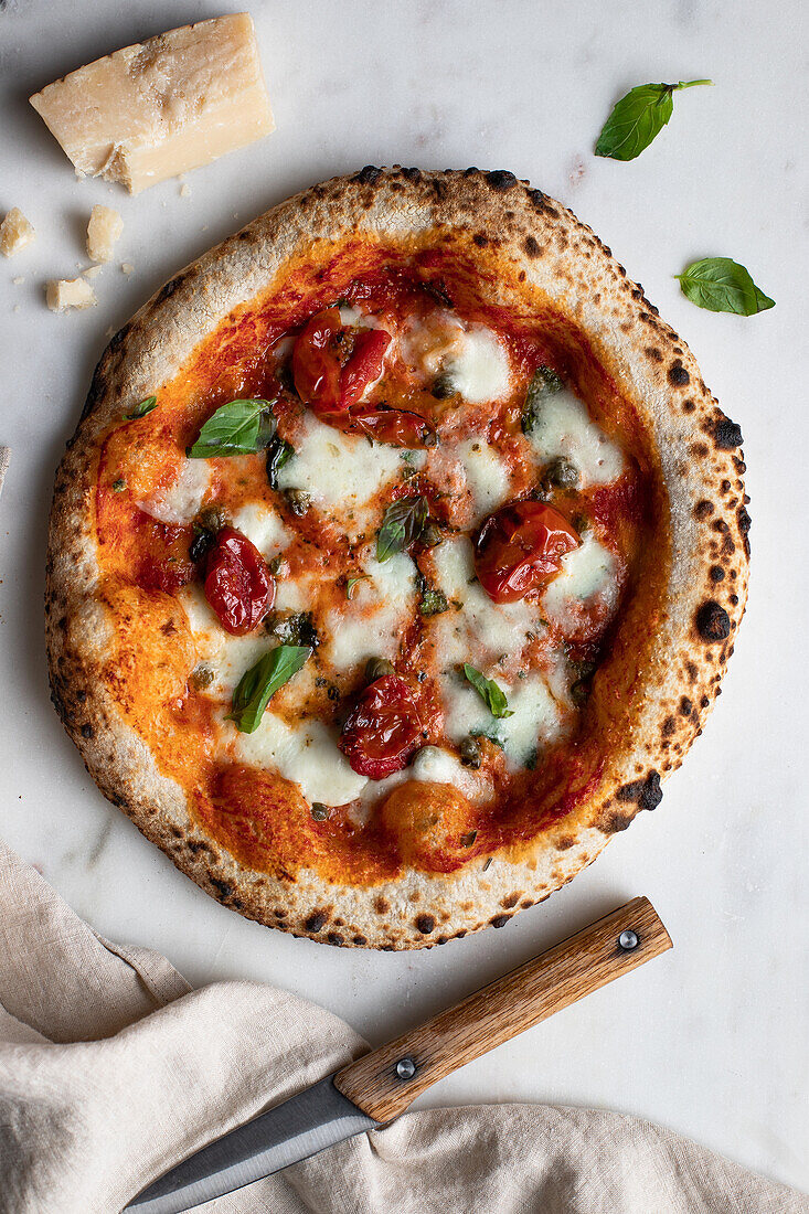 Draufsicht auf eine leckere Pizza mit Basilikum und Tomatensauce auf einem Holztisch neben einer Serviette in der Küche
