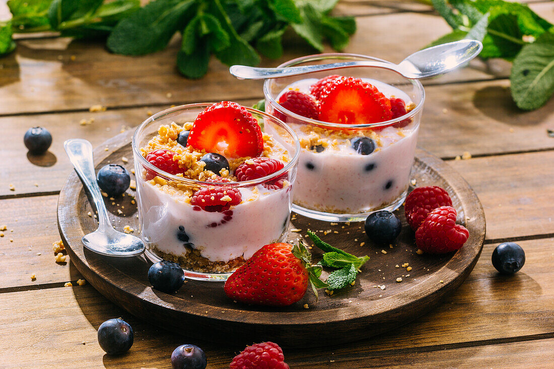 Köstlicher hausgemachter Joghurt mit Erdbeeren, Beeren und Müsli auf einem Holztisch im Hintergrund