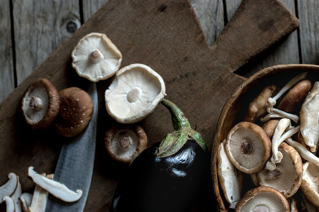 From above shot of wooden board with bowl full of shiitake mushrooms and eggplant on top