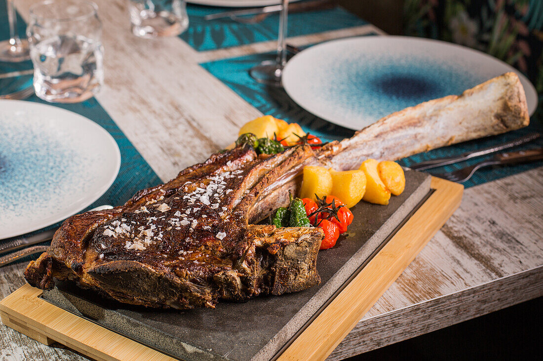 Tasty grilled ribeye beef steak with grains of salt and bright red and yellow tomatoes on served table