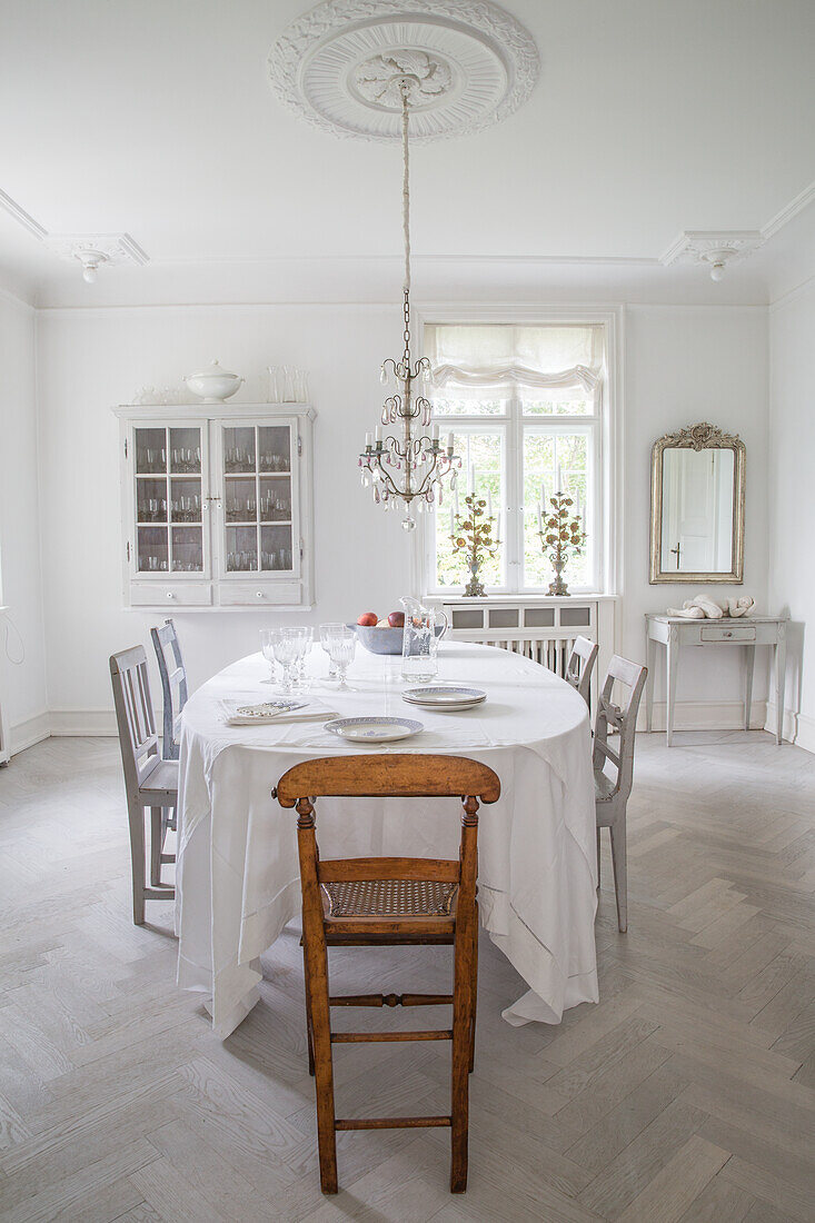 Bright dining area with wooden chairs, chandelier, stucco rosette and herringbone parquet flooring