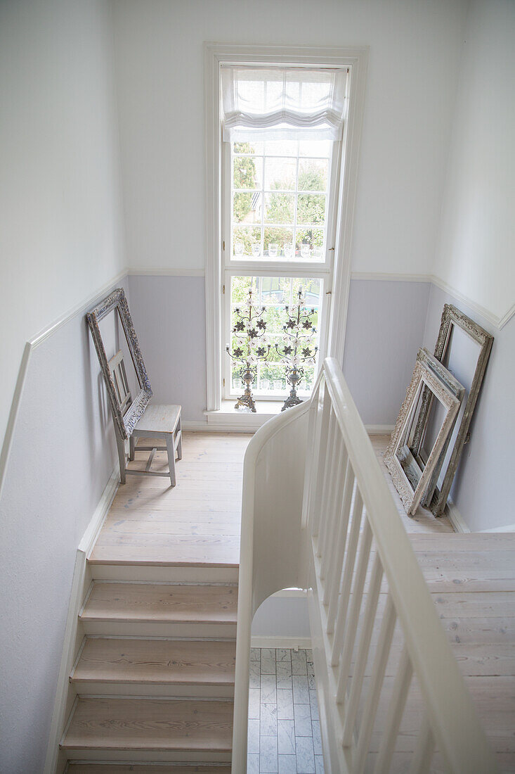 Light-colored wooden staircase with white walls and window, empty picture frame on the landing