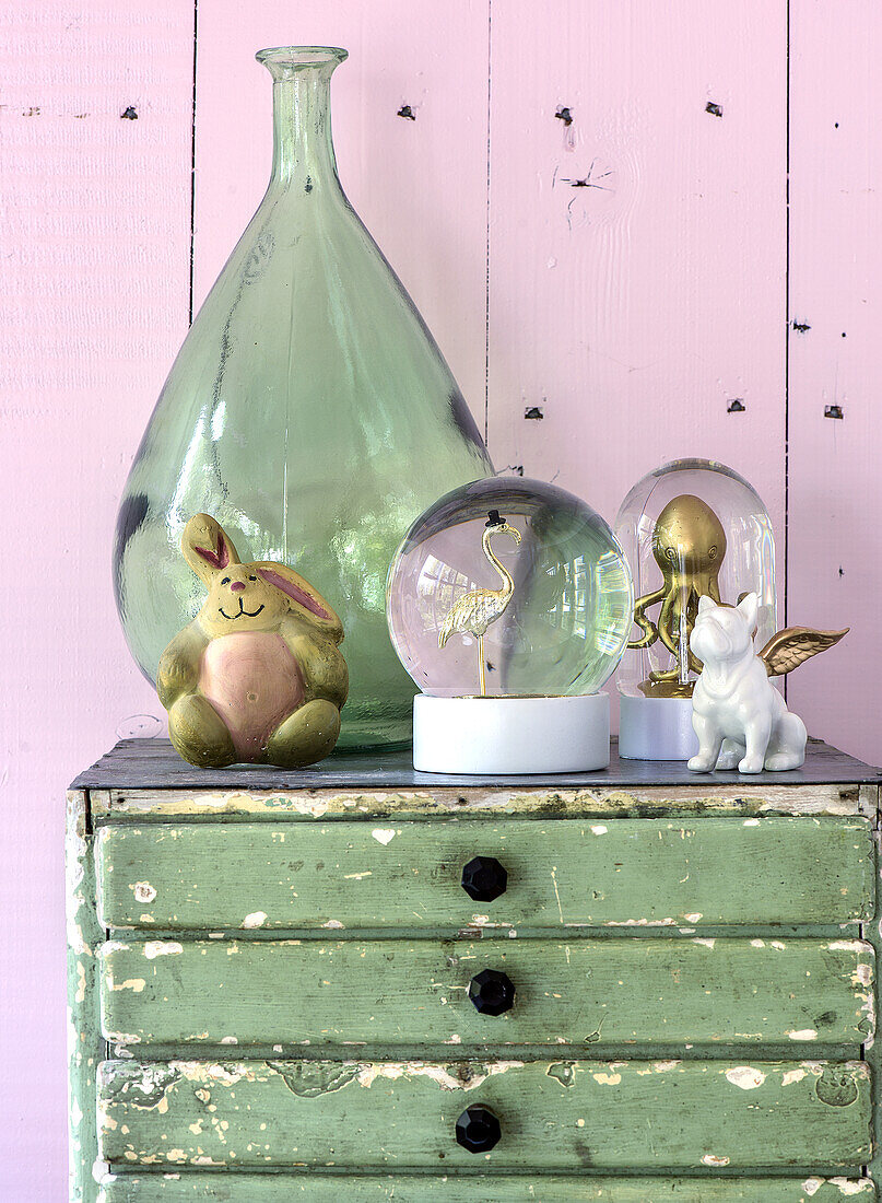 Decorative still life on a green chest of drawers with glass bottle, snow globes and ceramic figurines