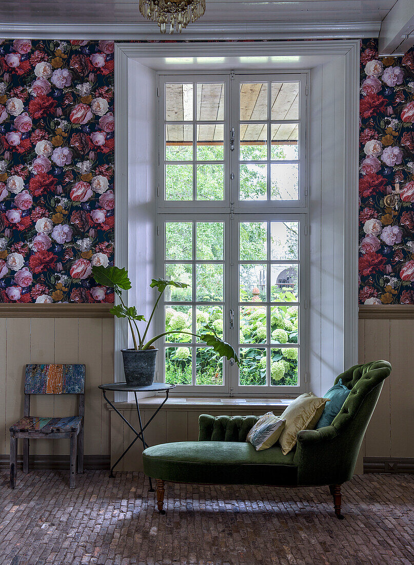 Green daybed in front of mullioned window, floral wallpaper and stone floor