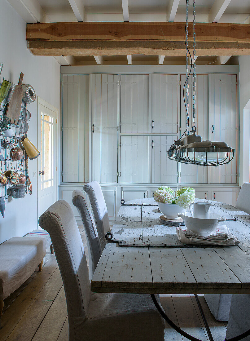 Rustic dining area with wooden table, elongated pendant light and white built-in cupboard