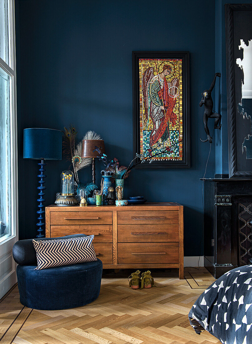 Wooden chest of drawers, mosaic picture and blue decorative objects in the bedroom