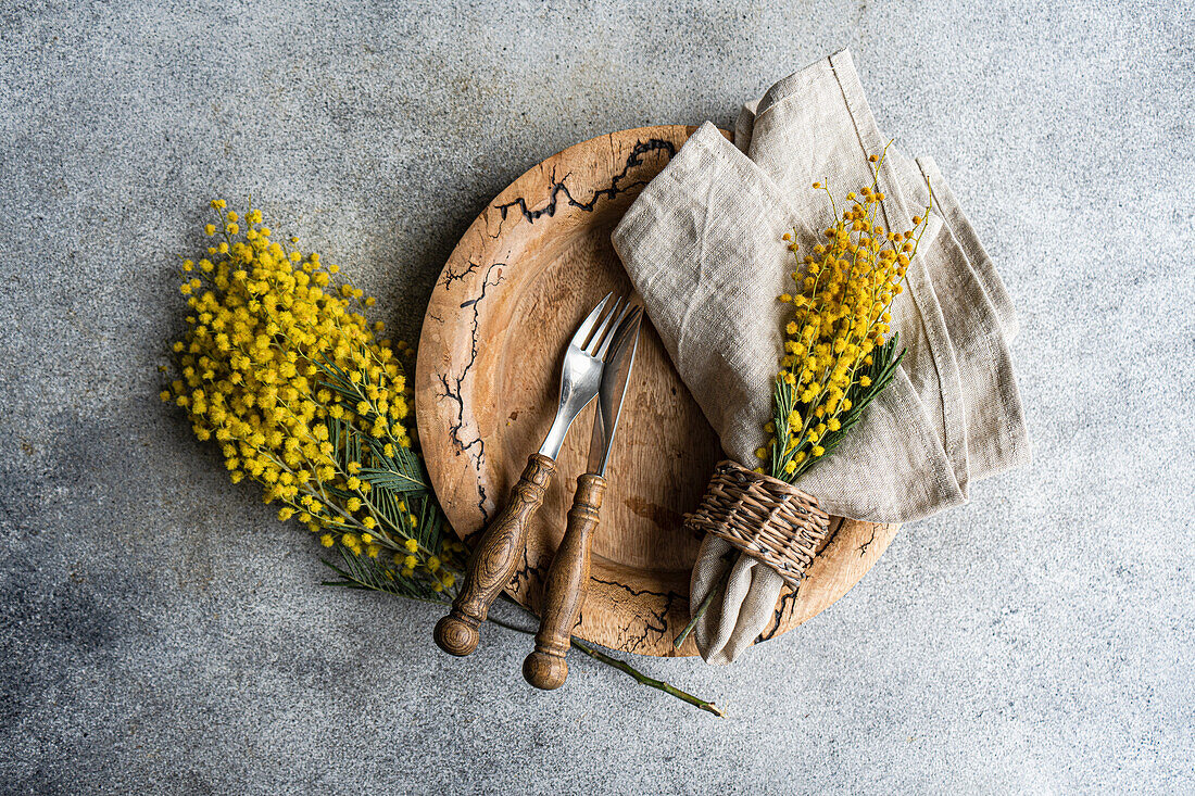 Rustikal gedeckter Tisch mit Mimosenzweigen (Acacia dealbata) auf grauem Betonhintergrund