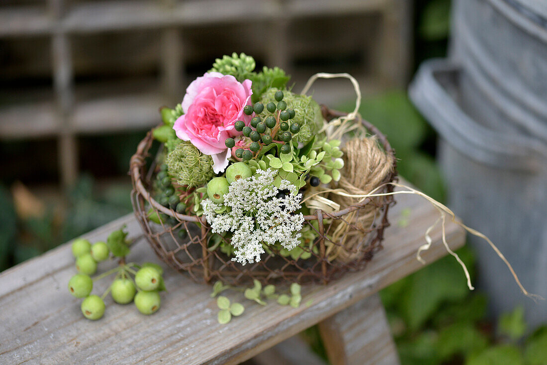Basket with rose blossom (pink), sedum, berries and ornamental apples on garden bench