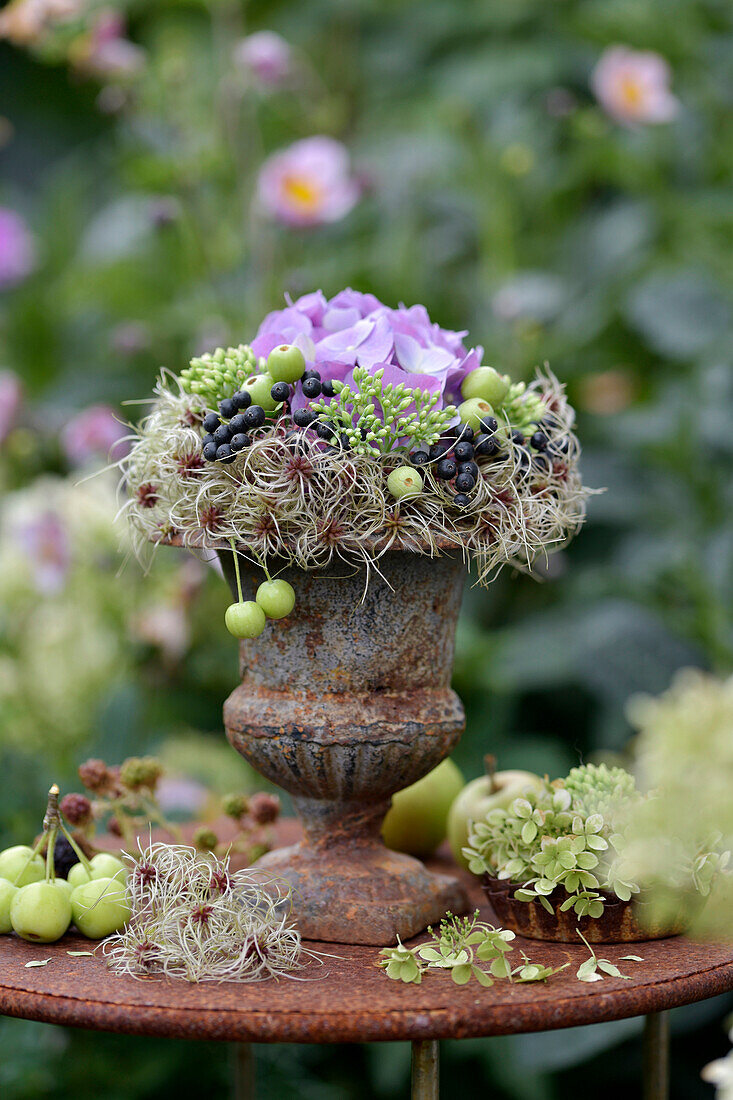 Late summer decoration in planter Late summer bouquet with hydrangea, sedum, berries and ornamental apples on garden table