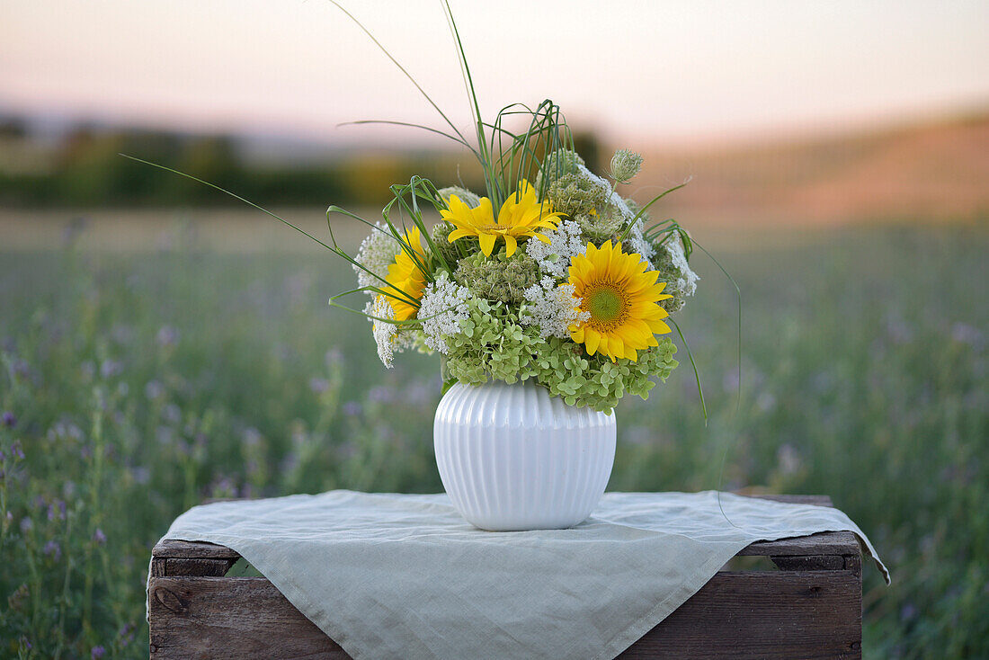 Spätsommerstrauß mit Hortensien (Hydrangea) und Sonnenblumen auf Gartentisch bei Sonnenuntergang