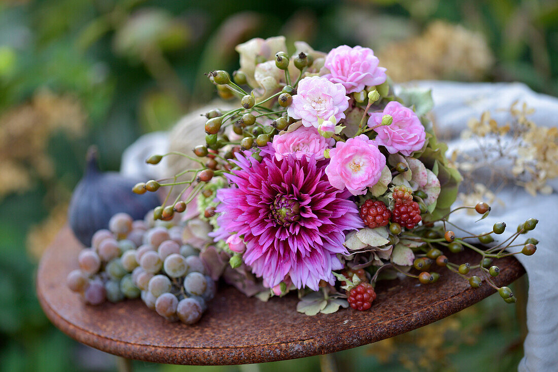 Spätsommerlicher Blumenstrauß mit Hortensien (Hydrangea), Dahlien (Dahlia), Rosen, Hagebutten und Brombeeren auf Metalltisch