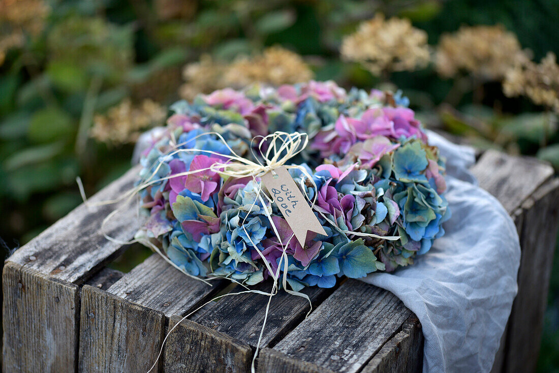 Bunter Hortensienkranz (Hydrangea) auf rustikaler Holzkiste im Garten