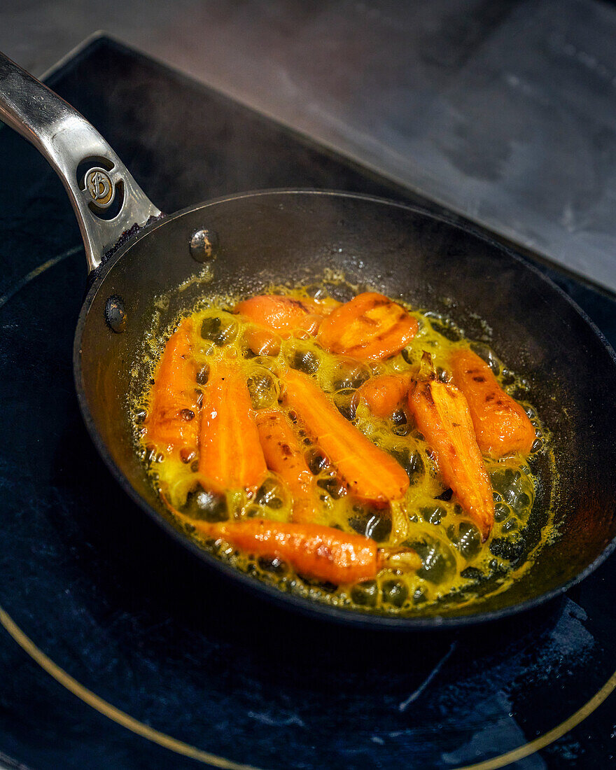 Karotten in einer Pfanne mit Kapern und Knoblauch sautieren