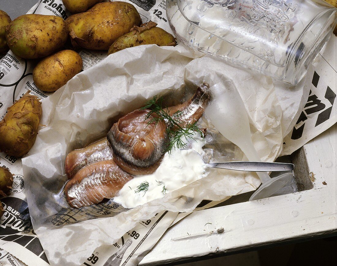 Matjesfilets mit Sahnesauce auf Papier, sowie Kartoffeln