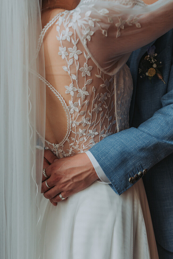 Bride in embroidered dress and groom in blue suit embrace each other