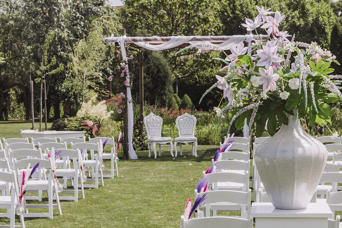 Freiluft-Trauungsbereich mit weißen Stühlen und Blumendekoration im Garten