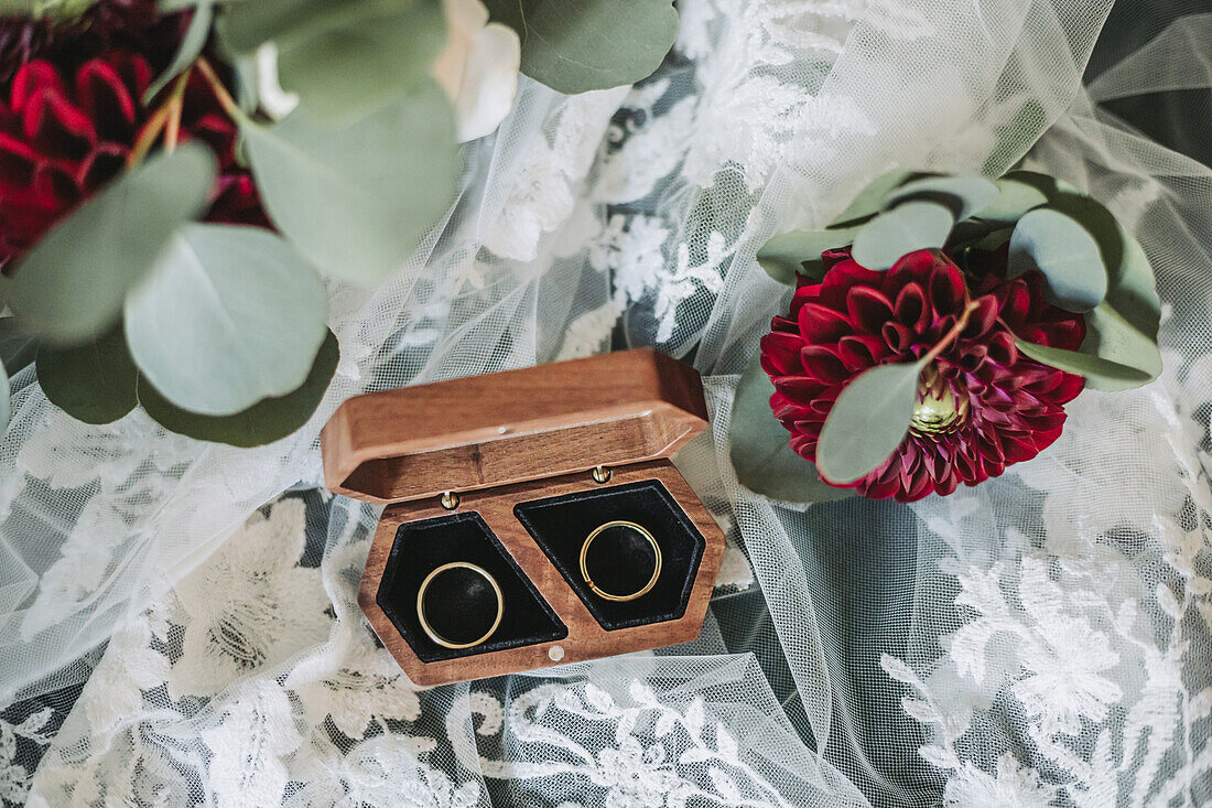 Wooden box with wedding rings next to dahlia on lace cloth