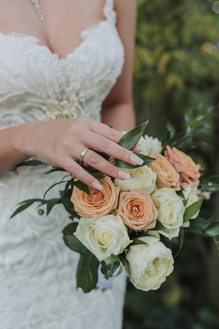 Bride with wedding ring holding bouquet of cream and peach roses