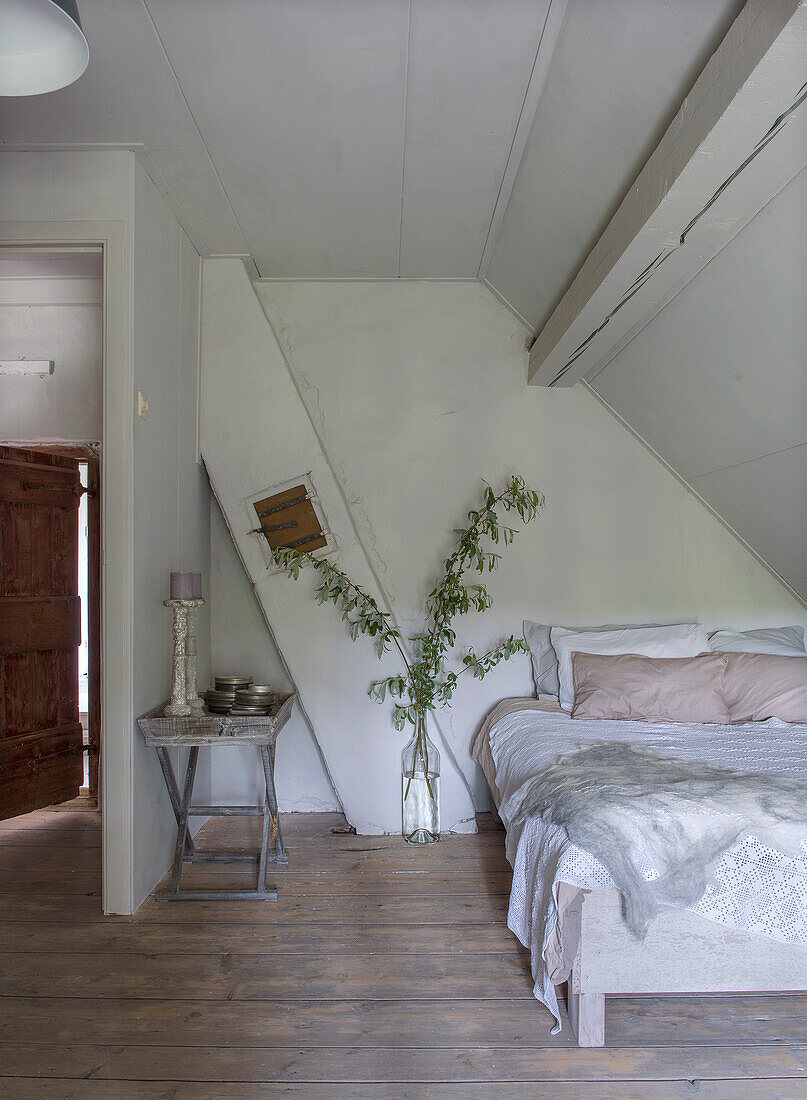 Bedroom with wooden floor and decorative branches, white wooden beams and sloping ceiling