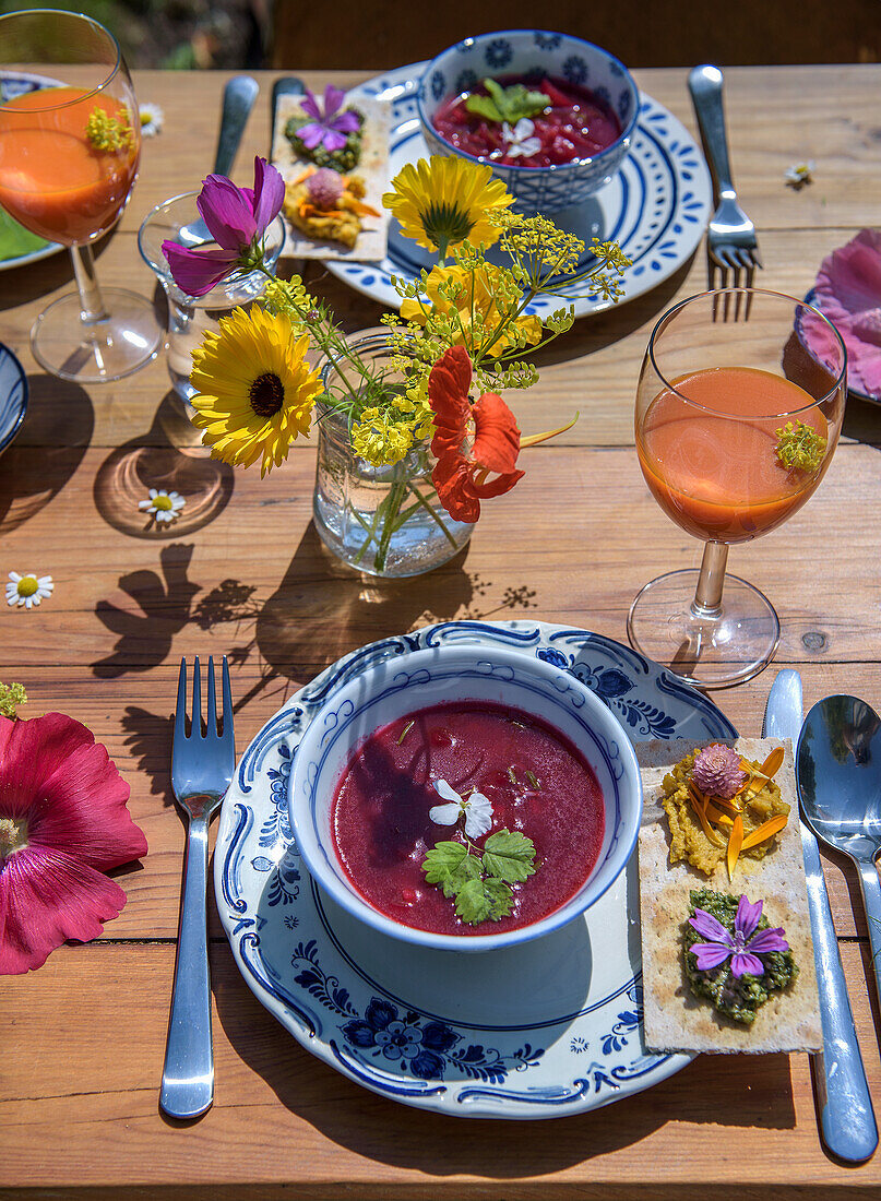 Sommerlicher gedeckter Tisch mit Blütendekoration und Rote-Bete-Suppe in Schalen