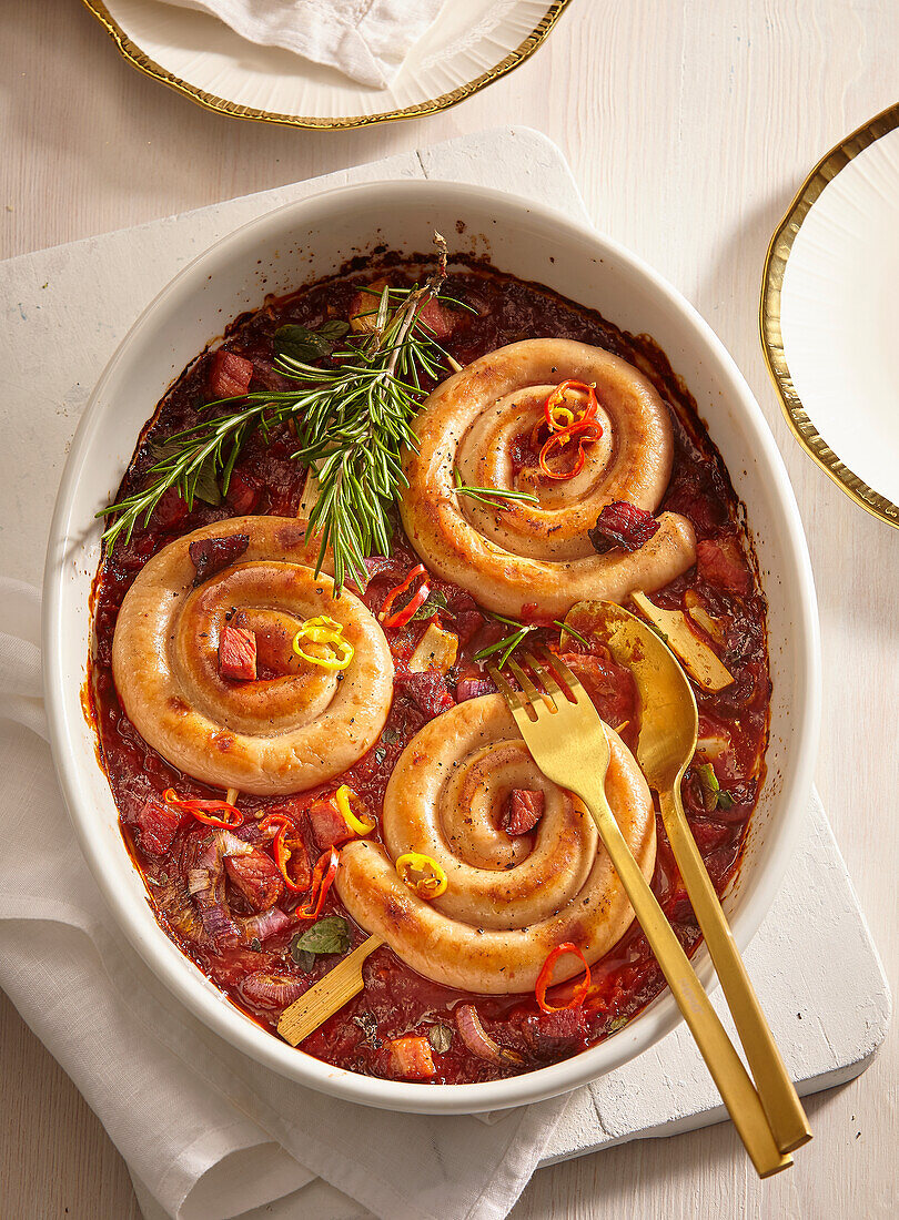 White sausage rolls in spicy tomato sauce with bacon and herbs