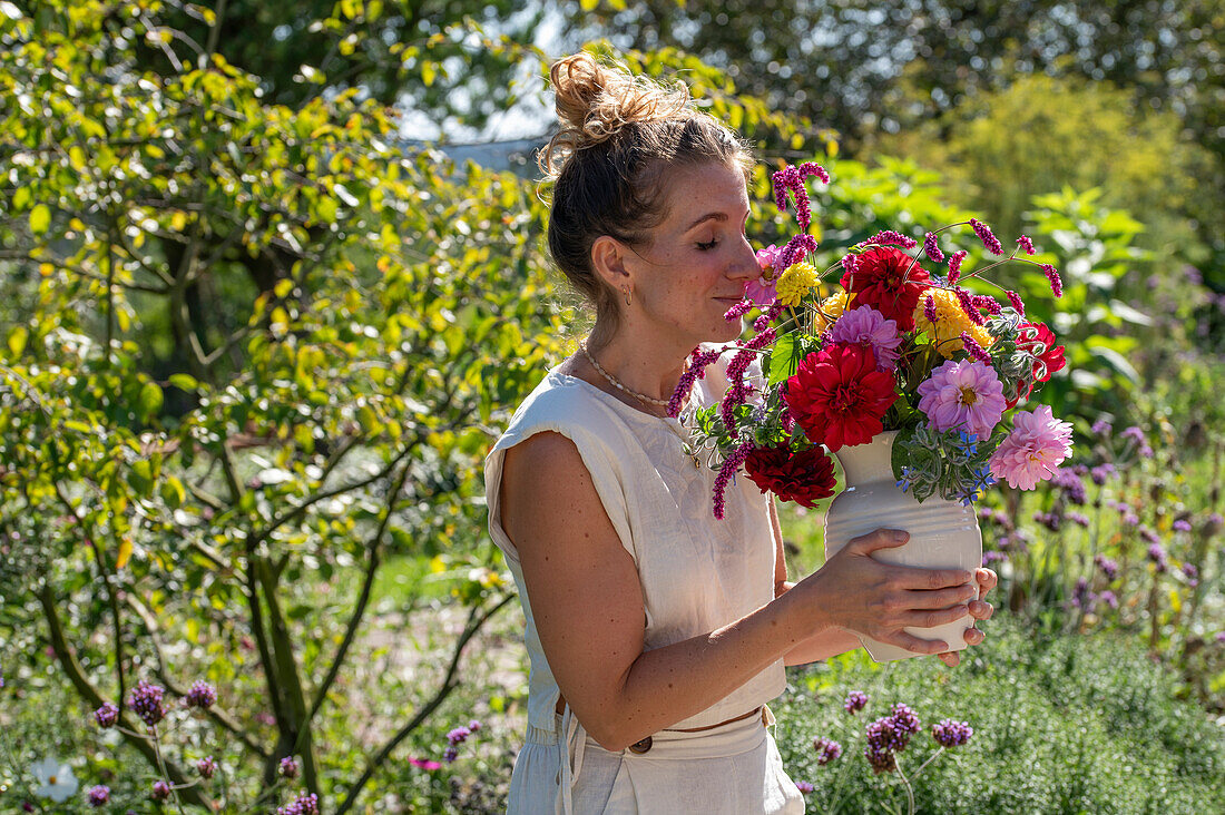 Woman smelling a colorful bouquet of dahlias (Dahlia), oriental knotweed (Persicaria orientalis), beard flower (Caryopteris), and borage