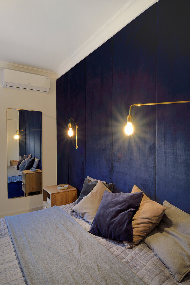 Dark blue wall paneling and golden wall lamps in the bedroom