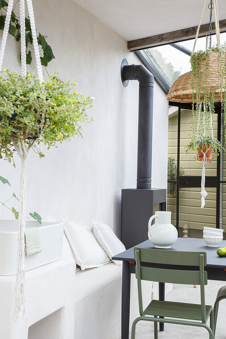 Conservatory with hanging plants, wood-burning stove and green garden chair