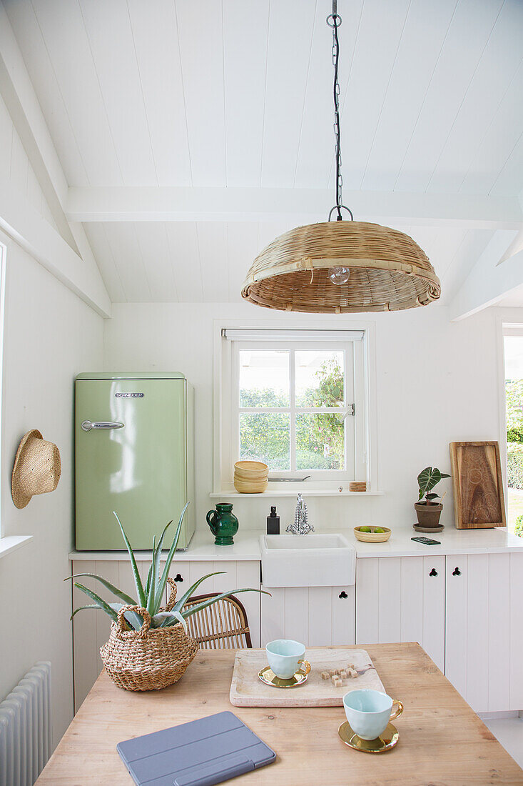 Kitchen with pastel green fridge and wicker lamp above wooden table