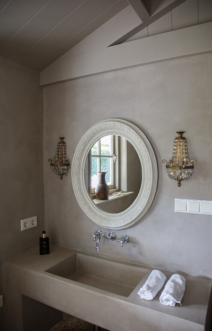 Round mirror with ornaments above modern washbasin in bathroom