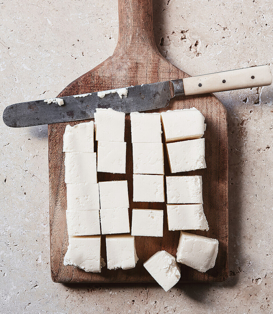 Portionierte Paneer-Stücke auf Holzbrett mit Messer