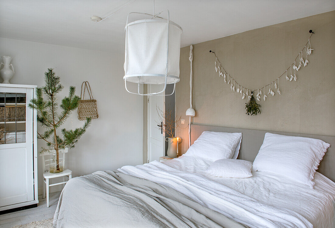 Bedroom in neutral tones with decorative plant, garland and white bed linen with grey bedspread