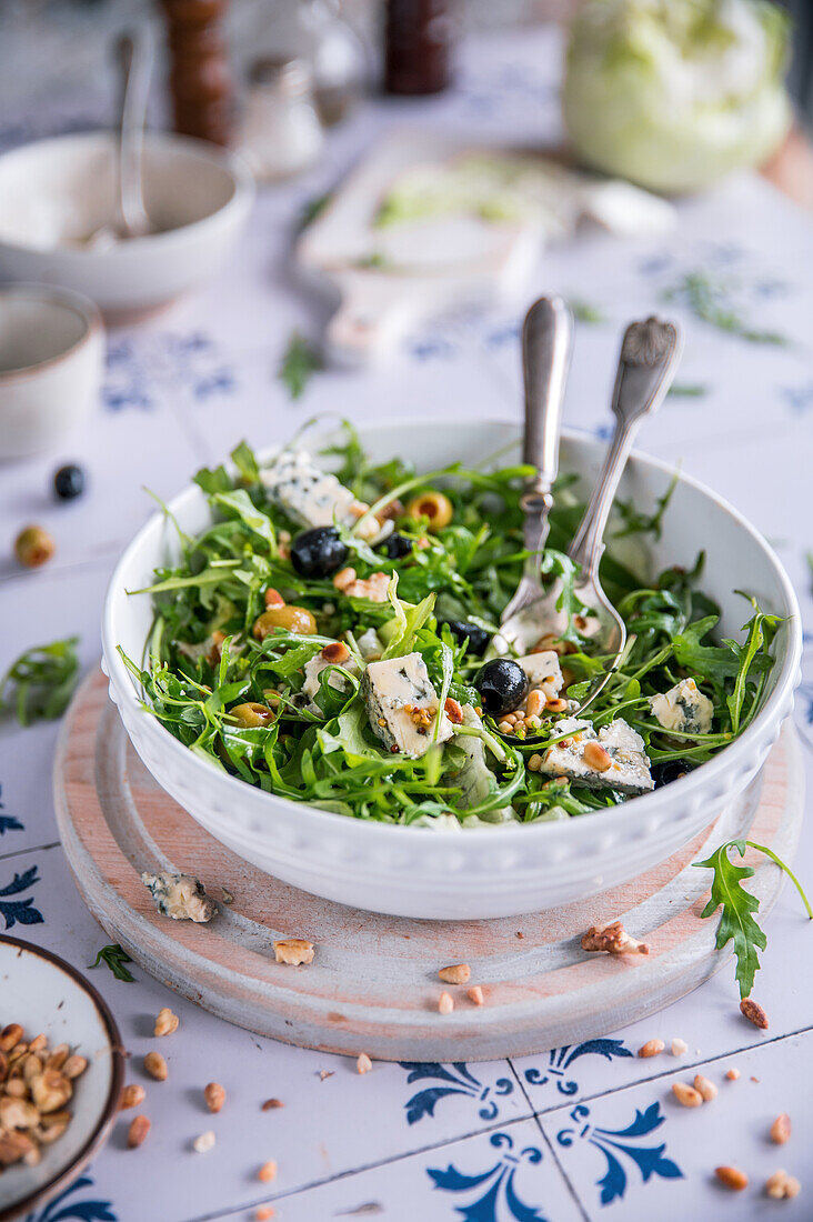 Rucolasalat mit Blauschimmelkäse, Oliven und gerösteten Pinienkernen