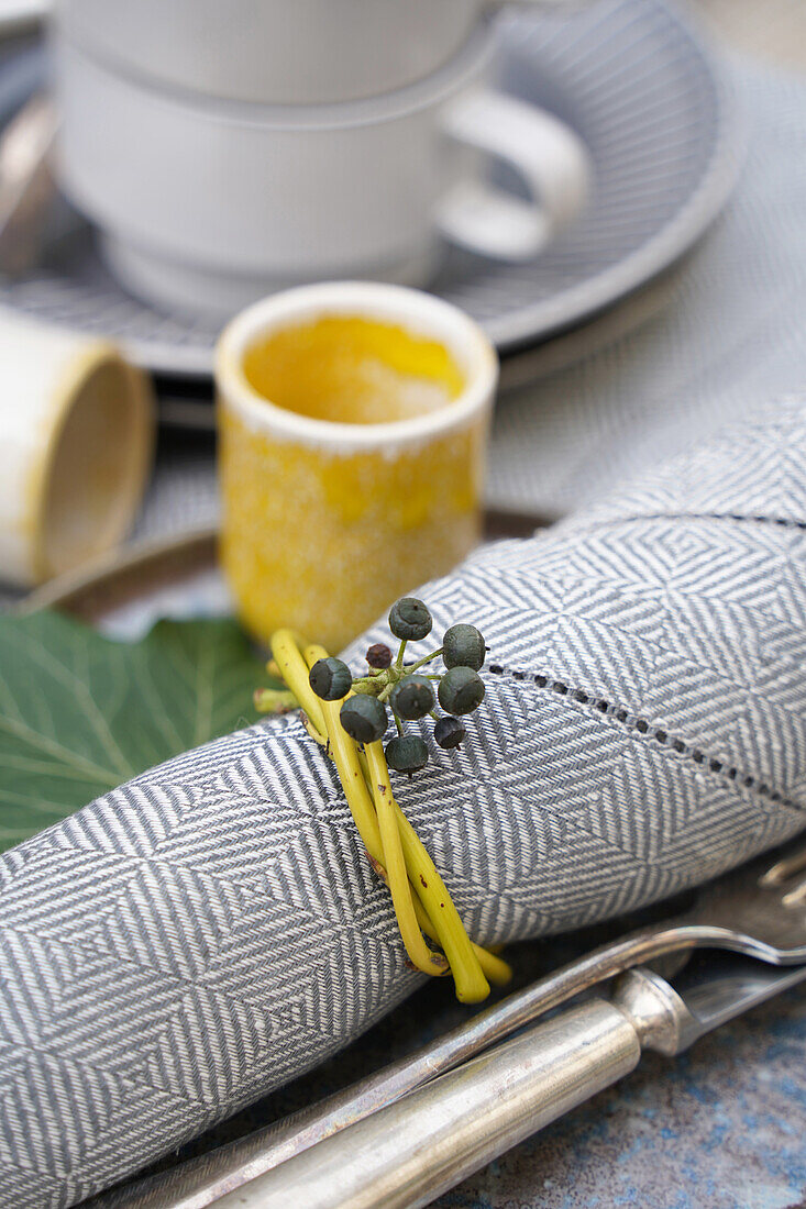 Table decoration with patterned cloth napkin, yellow napkin ring made of branches with ivy berries