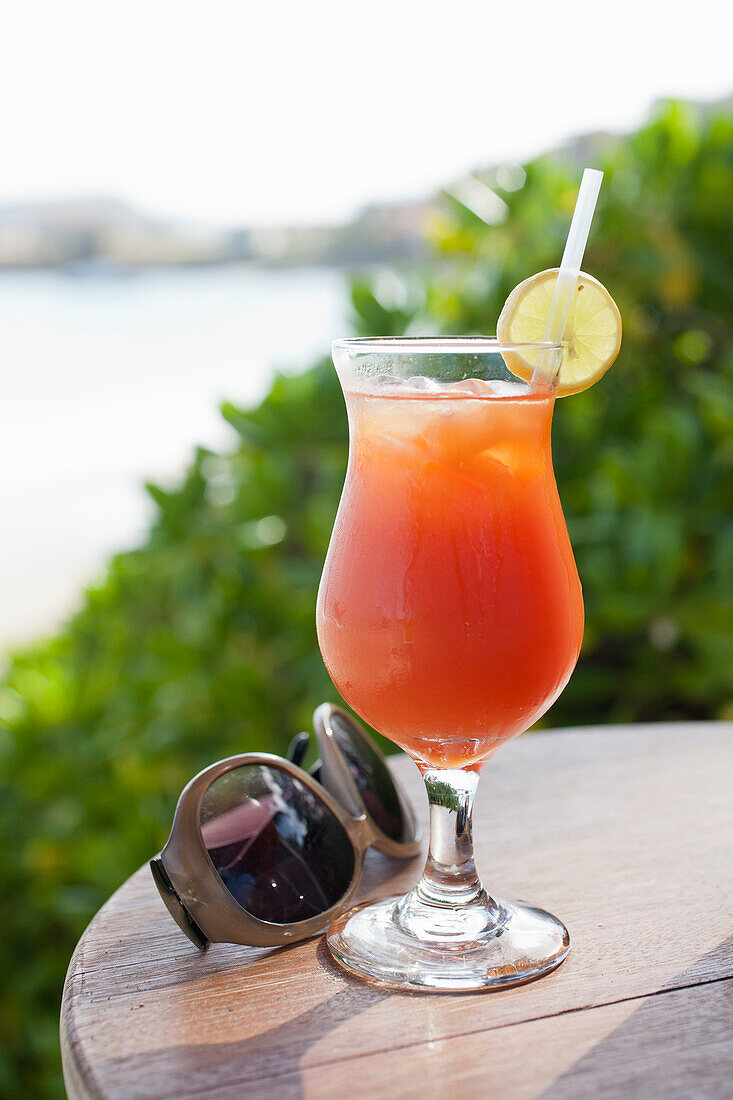 Summer cocktail with lemon slice and sunglasses on wooden table