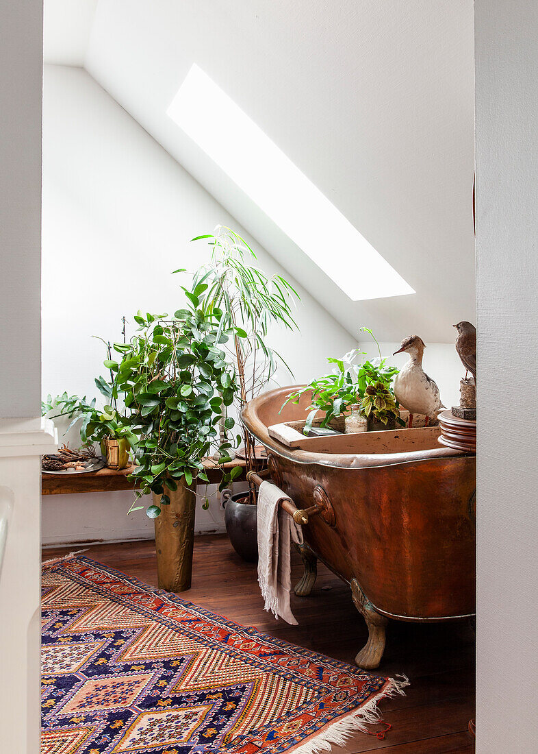 Copper bathtub with plants and oriental carpet in the bathroom under the sloping roof