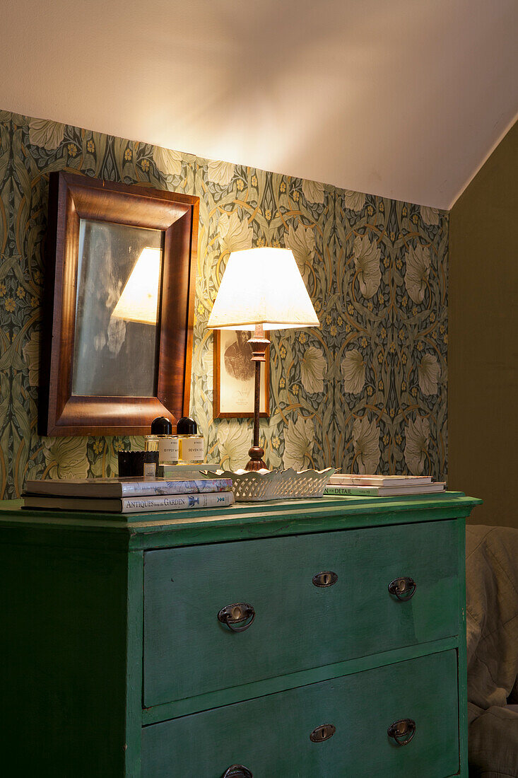 Green chest of drawers and table lamp in front of patterned wallpaper