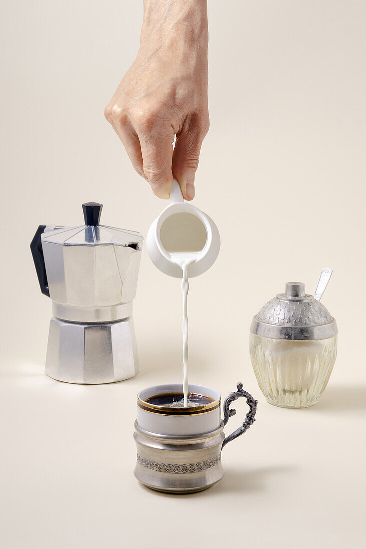 Milk being poured into a cup of espresso, espresso pot and sugar bowl next to it