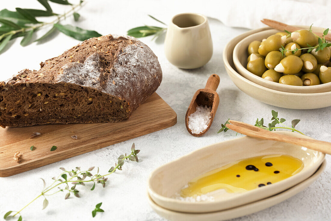 Rustikales Stillleben mit Vollkornbrot, Olivenöl und Mandeloliven