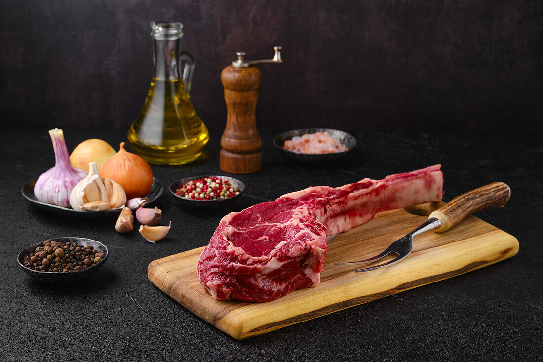 Raw cowboy steak with spices and herbs on cutting board