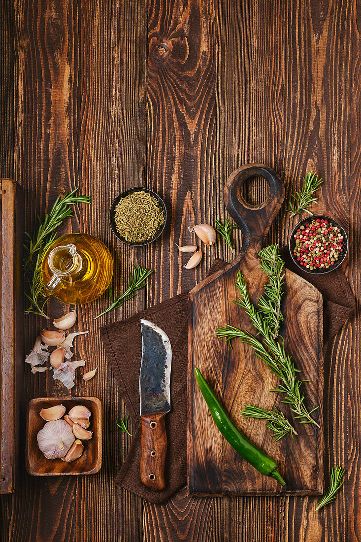 Stillleben mit Rosmarinzweigen, Knoblauch und Gewürzen auf Holzbrett