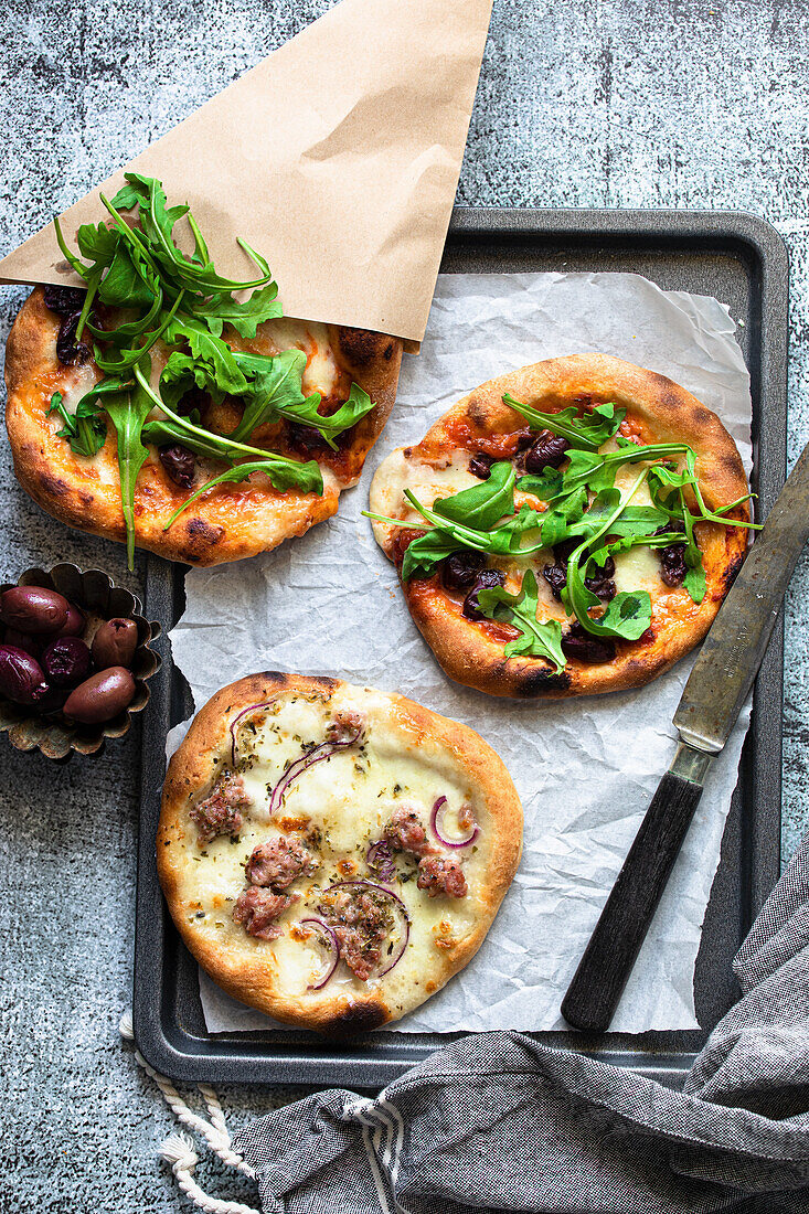 Mini pizzas with bacon, rocket, olives and red onions