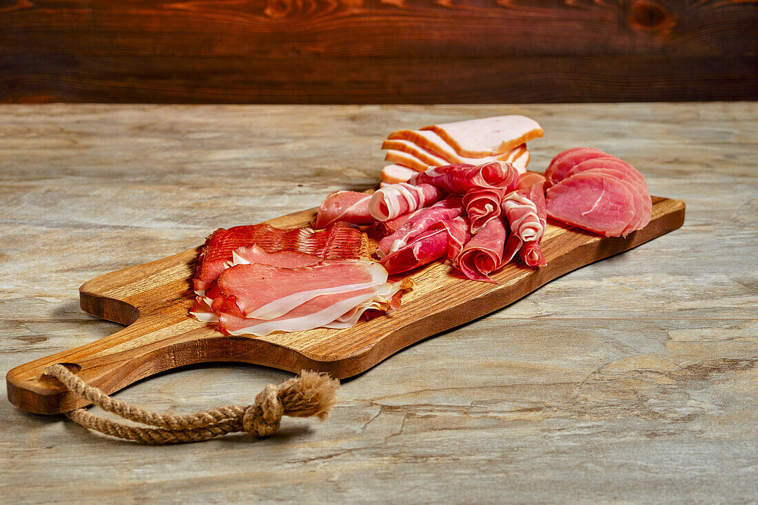 Various types of sausage and ham on a wooden board