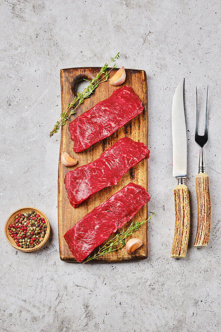 Raw beef steaks on wooden board with spices and cutlery