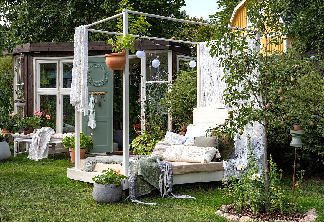 Gemütliche Gartenecke mit Sonnenbett, Kissen und Pflanzen im Sommer